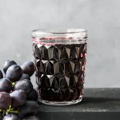 Szklanka ciemnego soku z winogron obok kiści świeżych winogron.