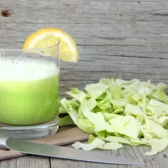 Szklanka zielonego soku z kapusty z plasterkiem cytryny, obok posiekana kapusta i nóż.